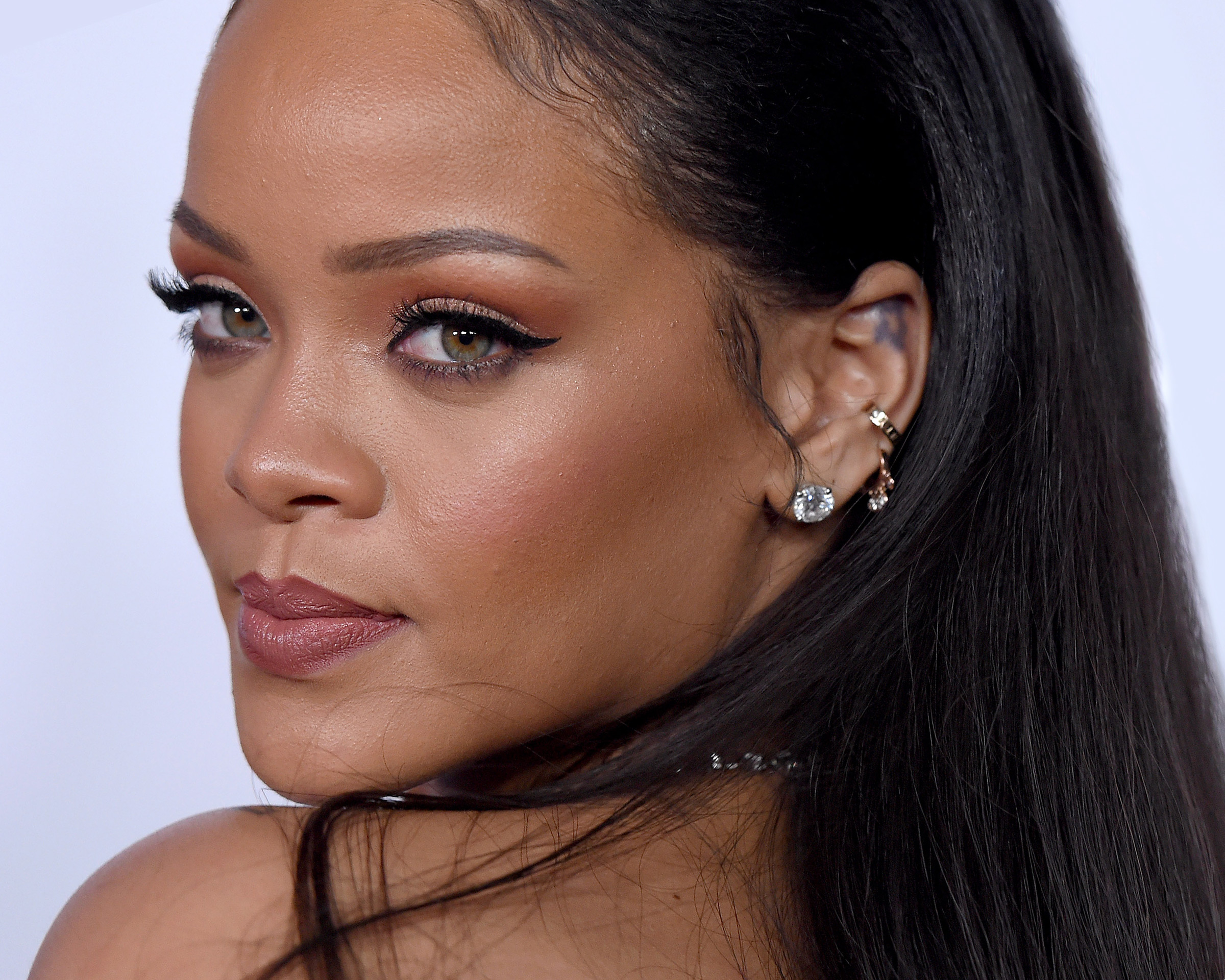 Cushion cut diamond stud earrings by Cartier, gold & diamond hoop earring, and gold ear cuff worn by Rihanna