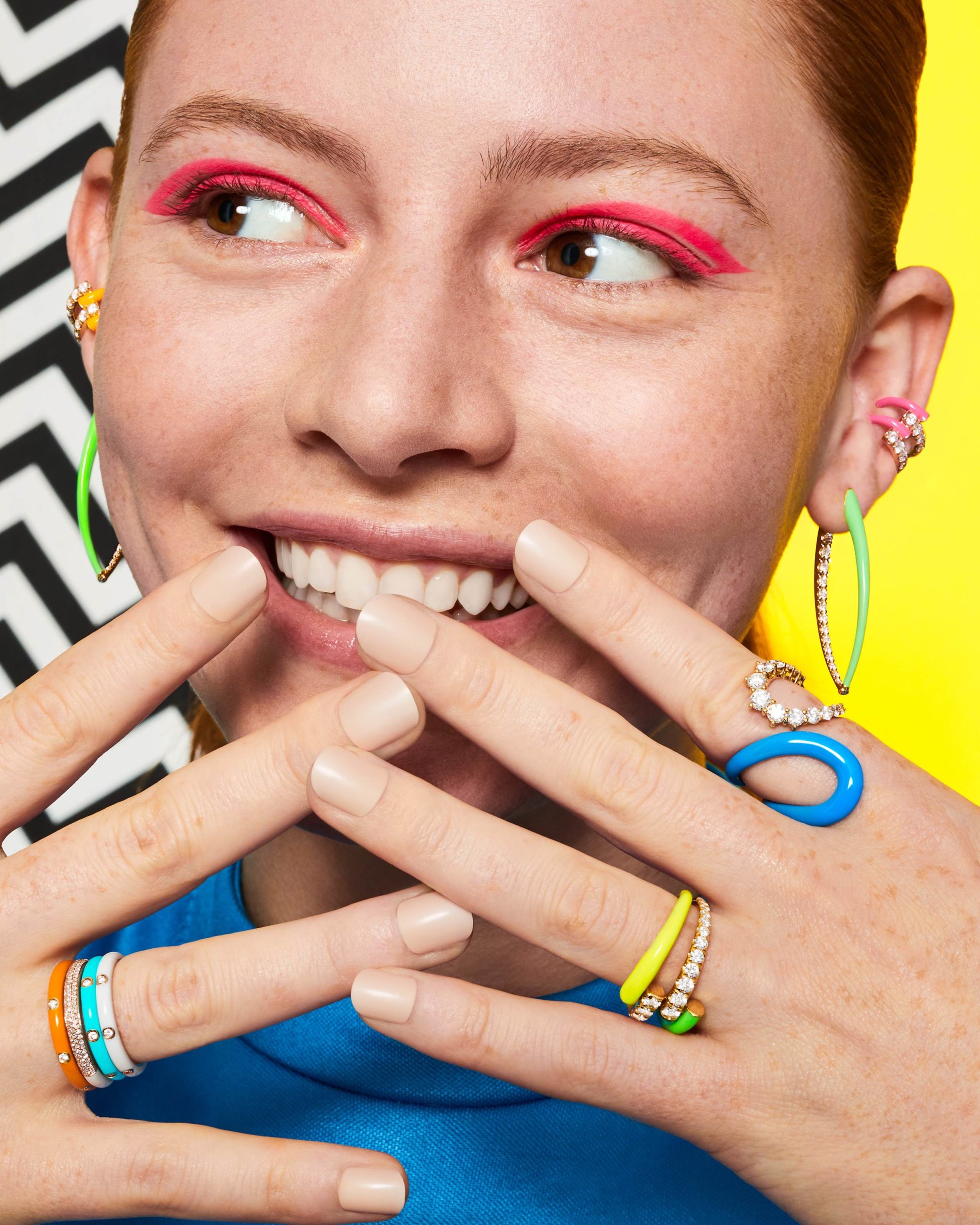 Woman wearing colorful enamel and diamond stackable on both hands, green enamel diamond hoop earrings and a pink enamel diamond ear cuff